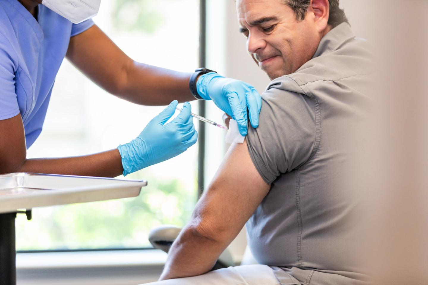 A clinician administers a vaccine to a middle-aged man