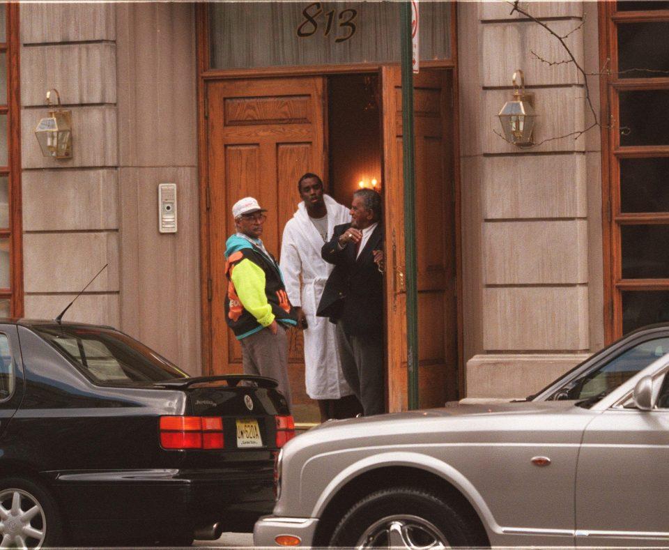 Sean Combs, wearing a bathrobe, and two other men standing outside a wooden door.