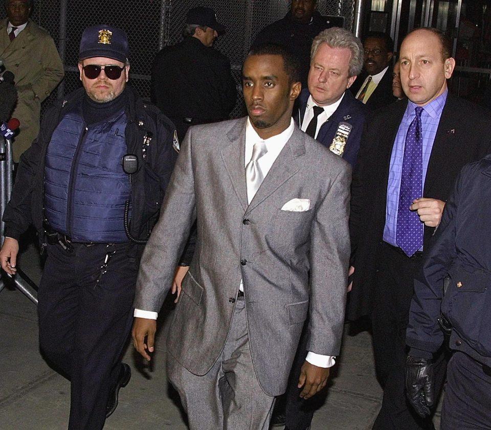 Sean Combs, wearing a suit, walking with three men standing behind him.