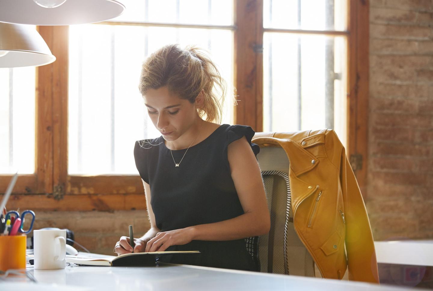 young professional sitting at a desk writing in a book