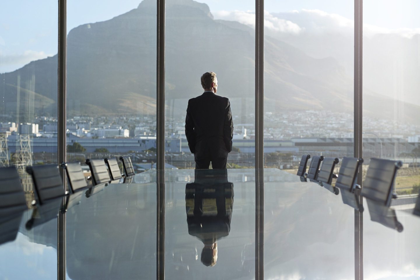 male office worker gazing out of a large office window in an empty meeting room