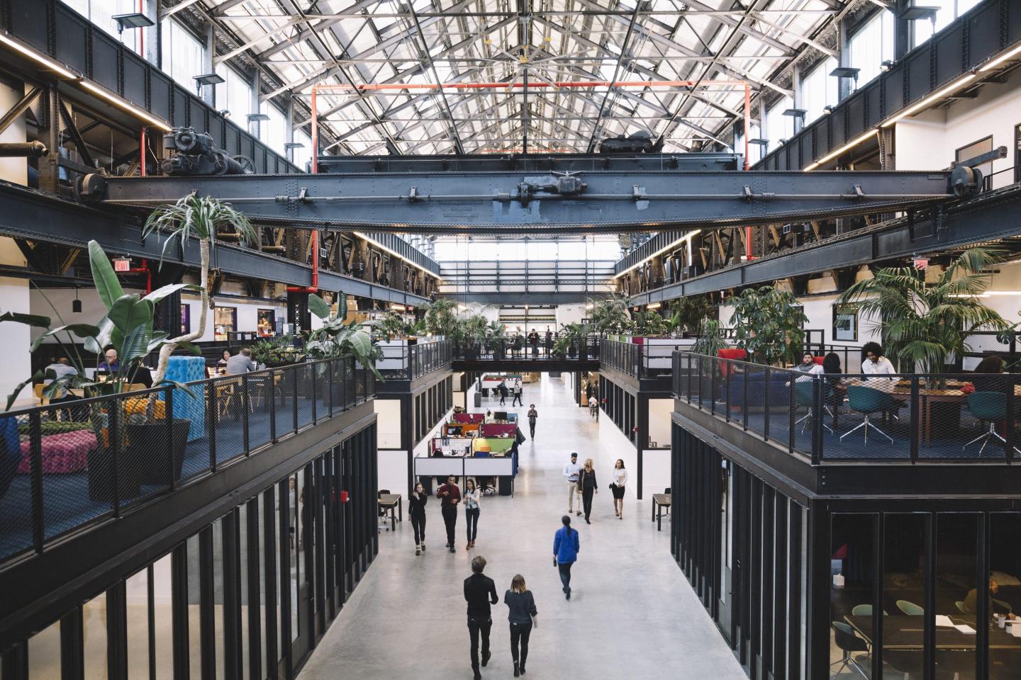 wide angle shot of Newlab's New York hub, an airy building with elevated office and desk space and people walking on a polished concrete walkway