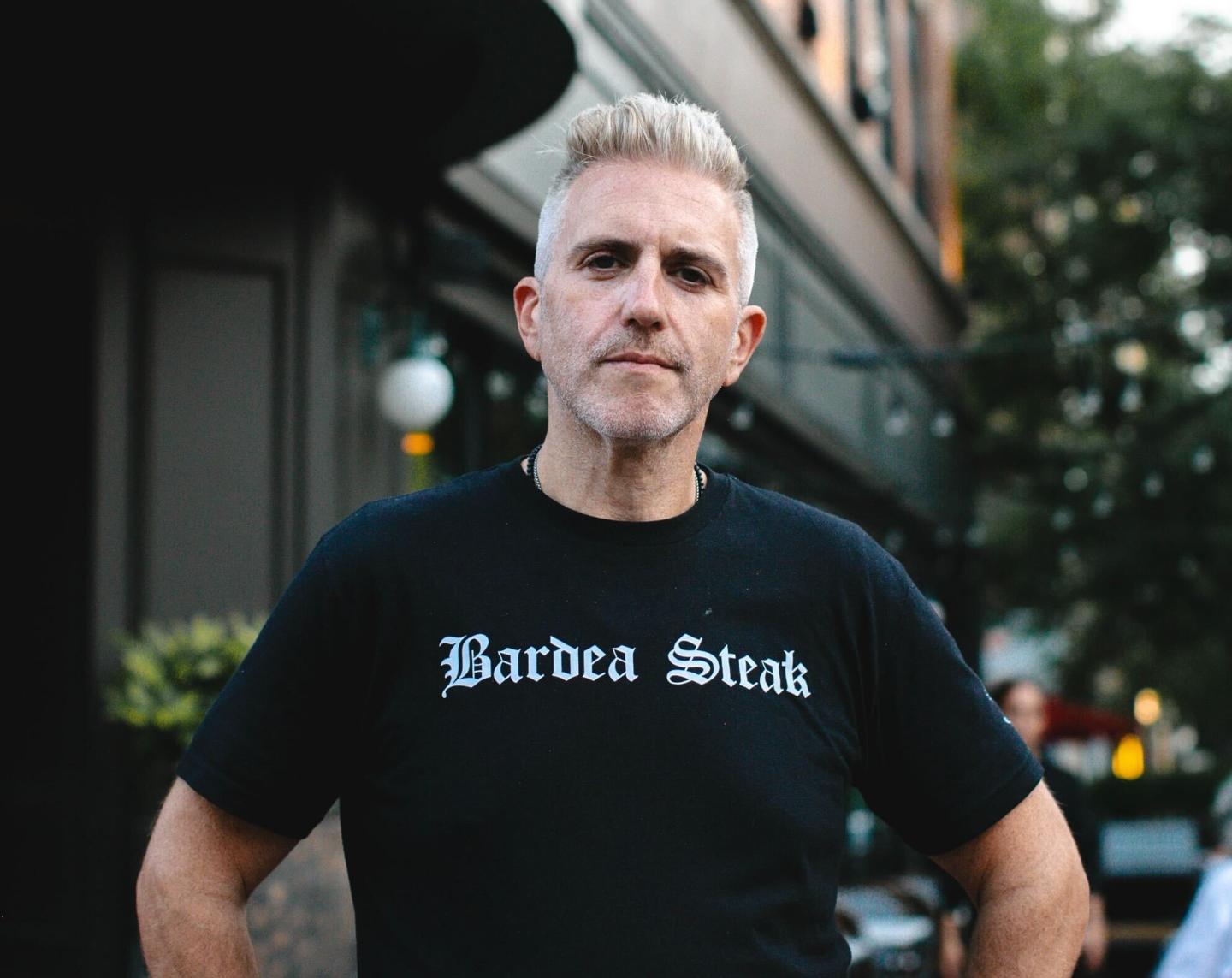 Scott Stein, wearing a black shirt with "Bardea Steak" spelled out in white letters, poses for a headshot.