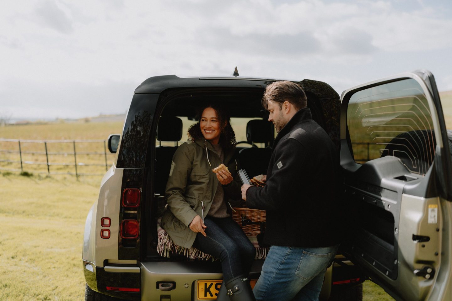 A millennial couple sits in the boot of a Jaguar Land Rover car.