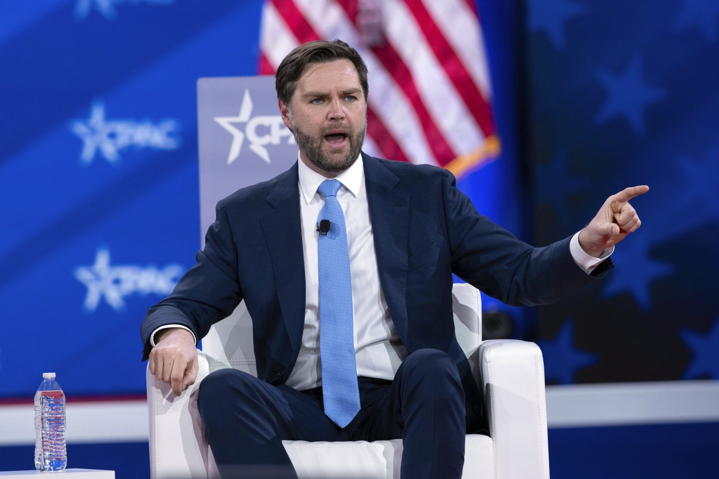 JD Vance sits in a chair at CPAC and points a finger into the audience