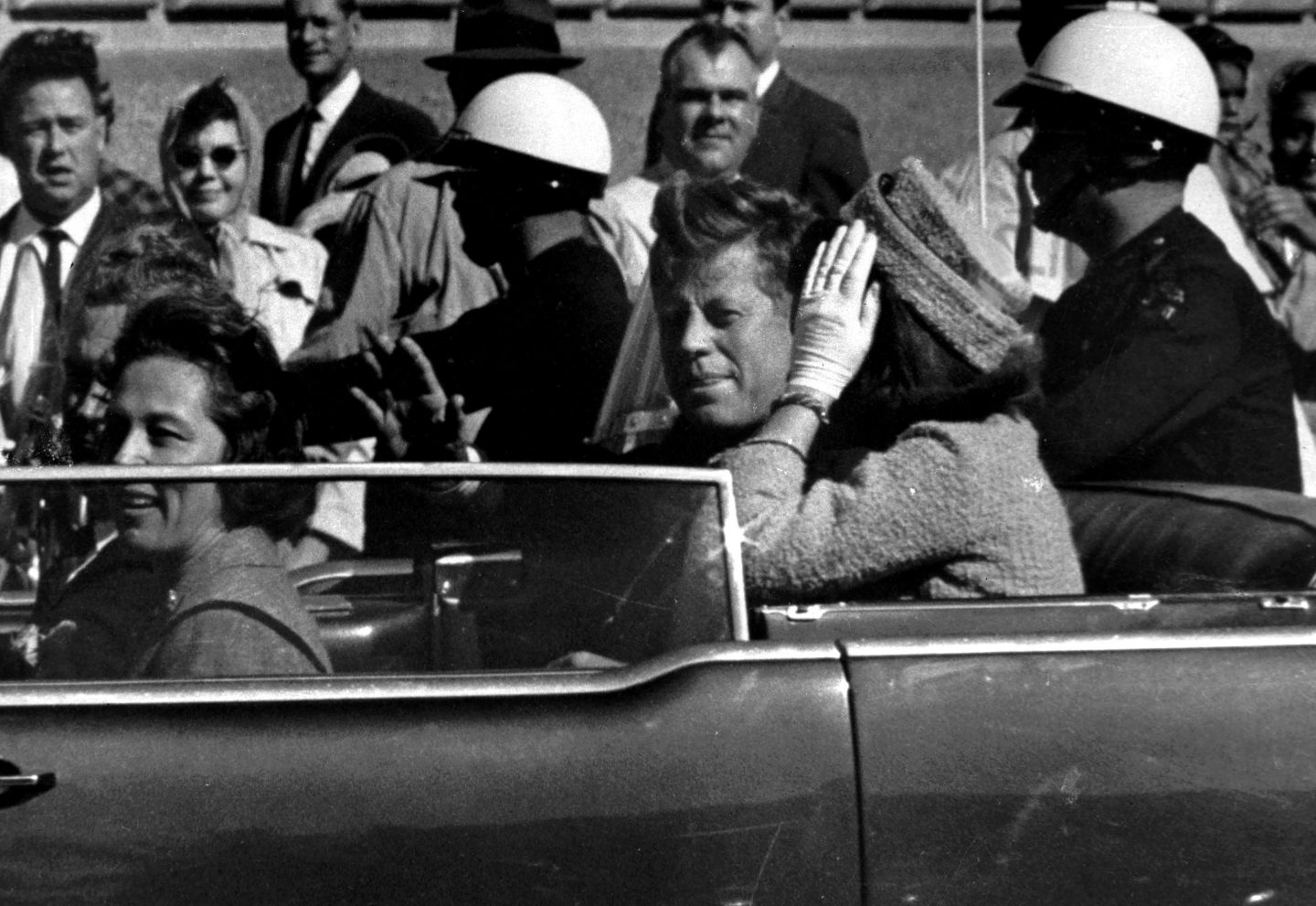 President John F. Kennedy waves from his car in a motorcade approximately one minute before he was shot, Nov. 22, 1963, in Dallas.