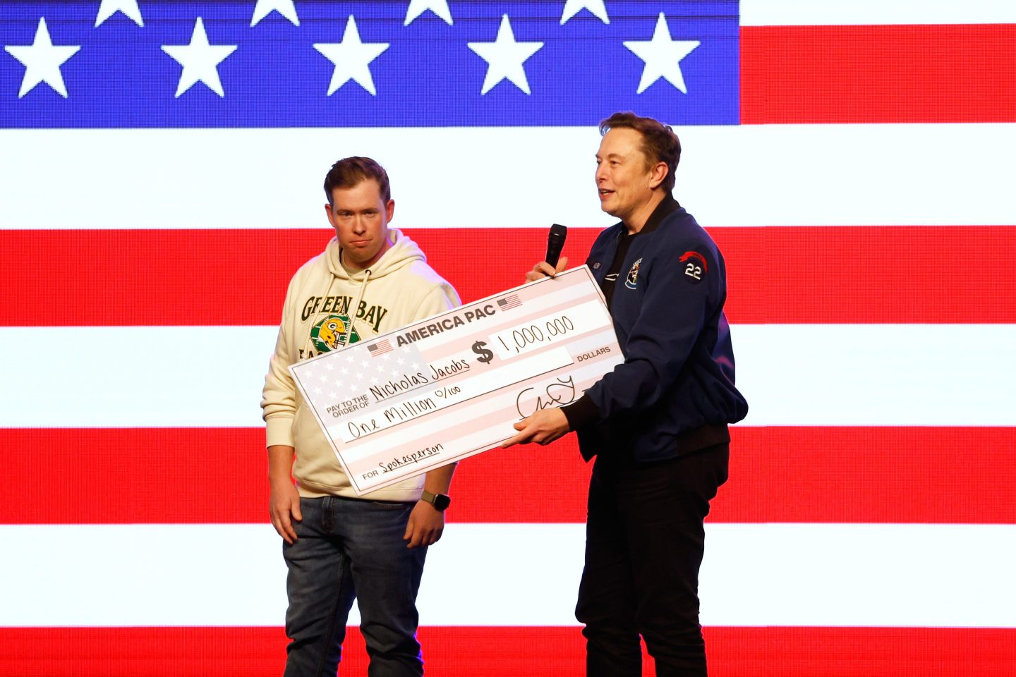 Elon Musk presents a check for $1 million dollars during a town hall on March 30, 2025, in Green Bay, Wis.