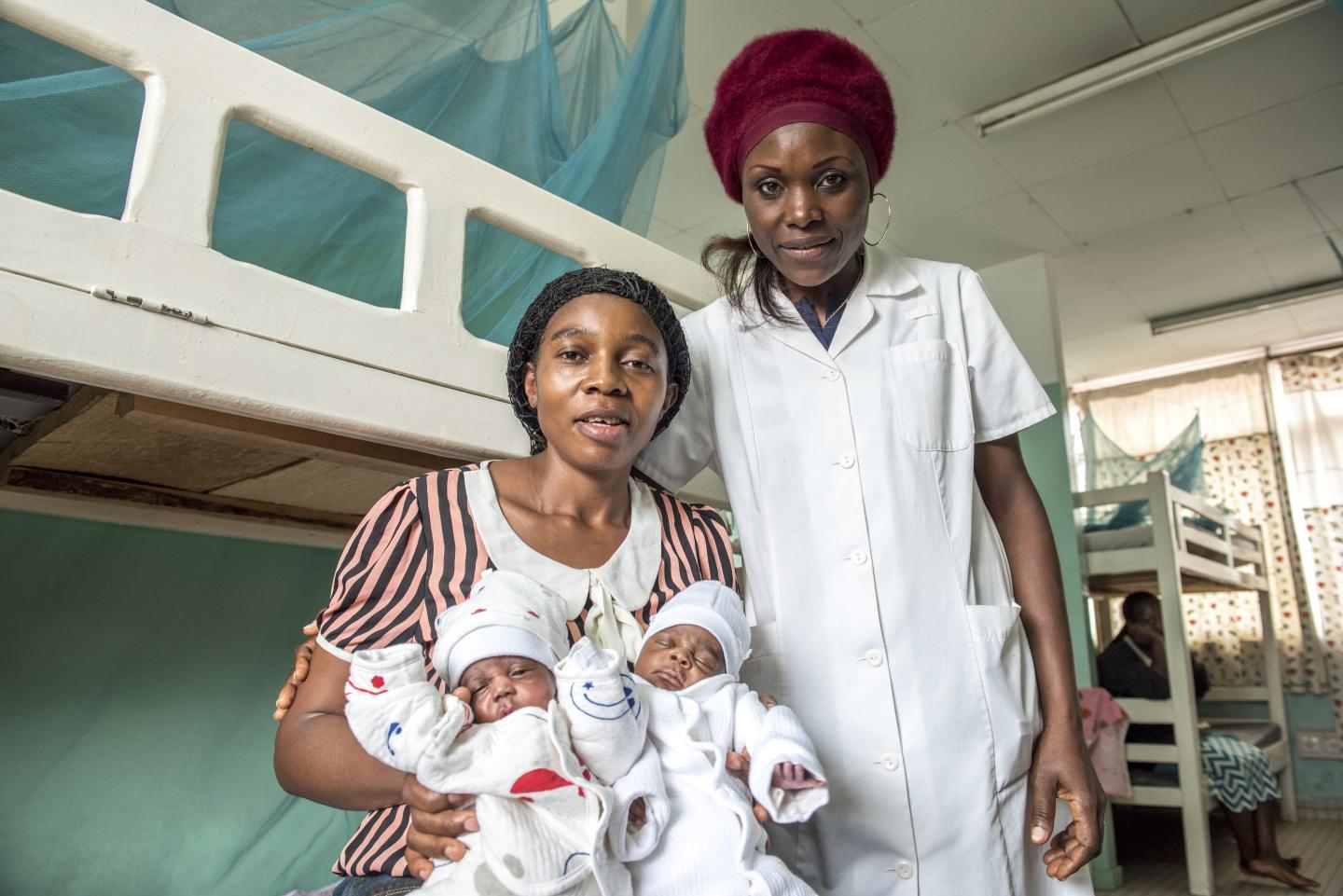 A woman with two babies sits beside a nurse in hospital.