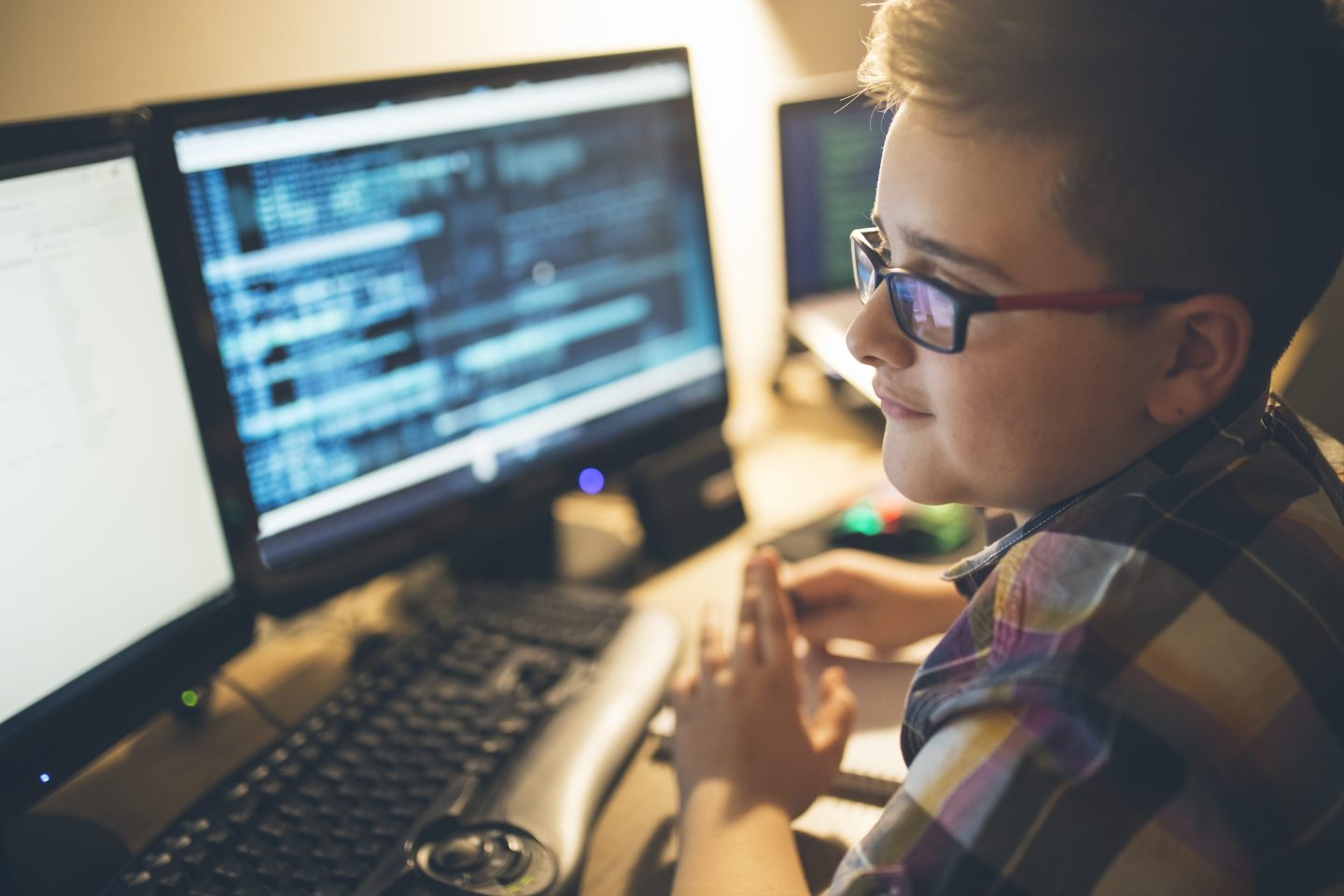 A young boy looks at two dual computer monitors