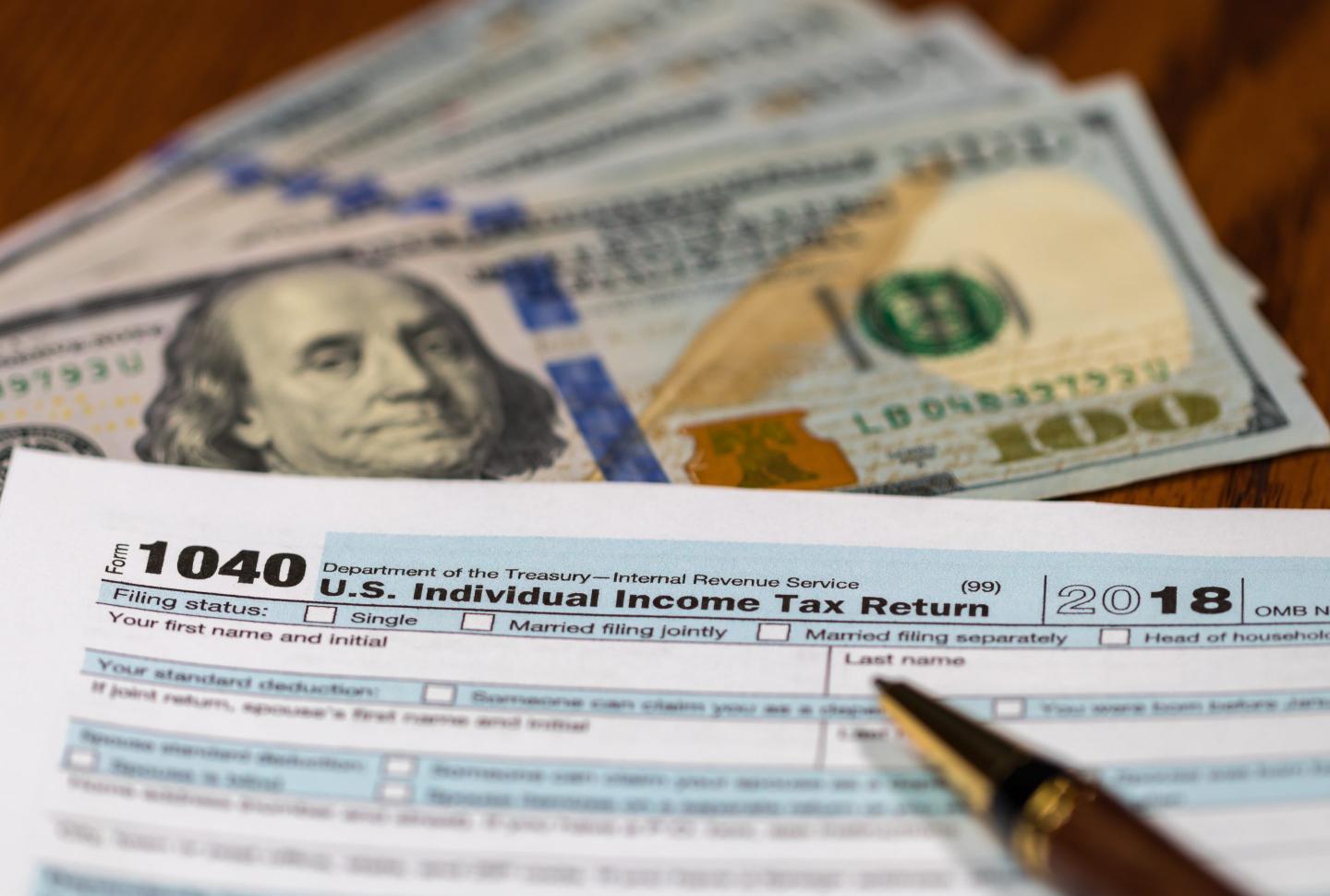 IRS Form 1040 next to 100-dollar bills