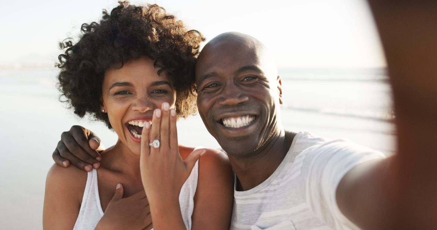 Happy male-female couple with the woman showing an engagement ring on her finger