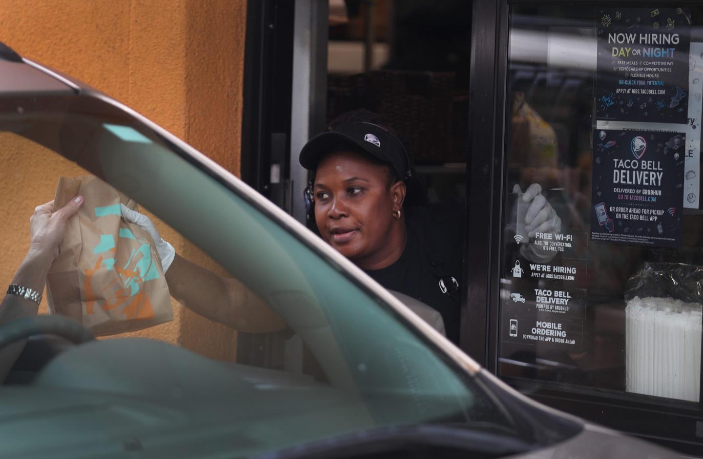 A Taco Bell workers hands a bag to a customer in their car.