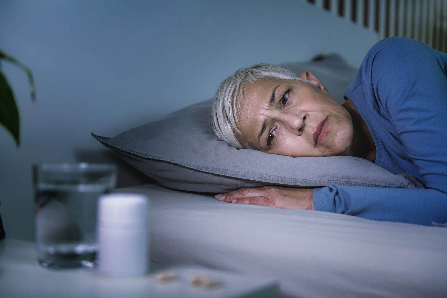 Older woman lying awake in bed, facing camera with her eyes open