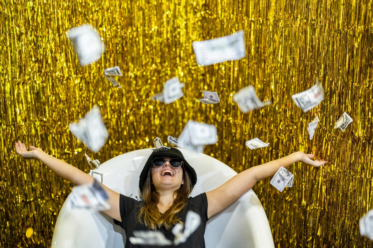 Carefree woman lying in bathtub with arms outstretched amidst falling money