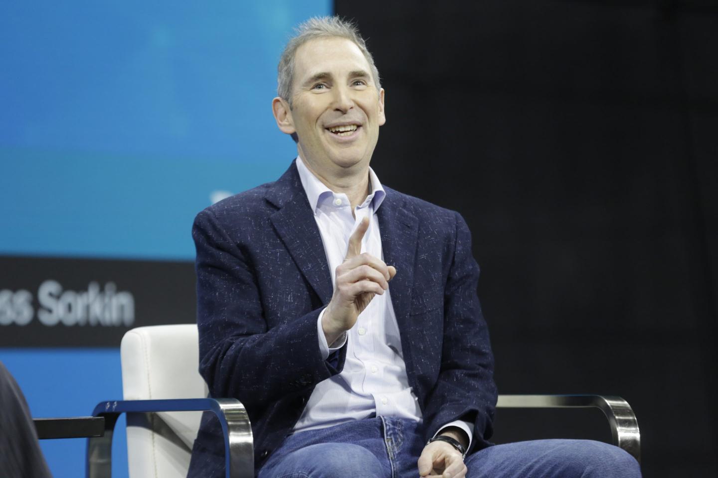 Amazon CEO Andy Jassy smiles while sitting in a chair