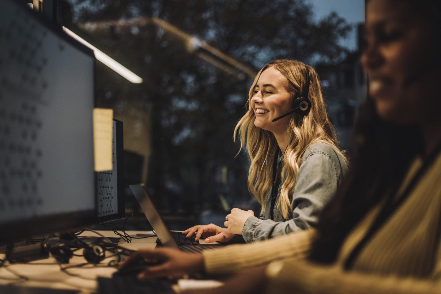 A photo of a woman at a desk talking to other people on her computer.