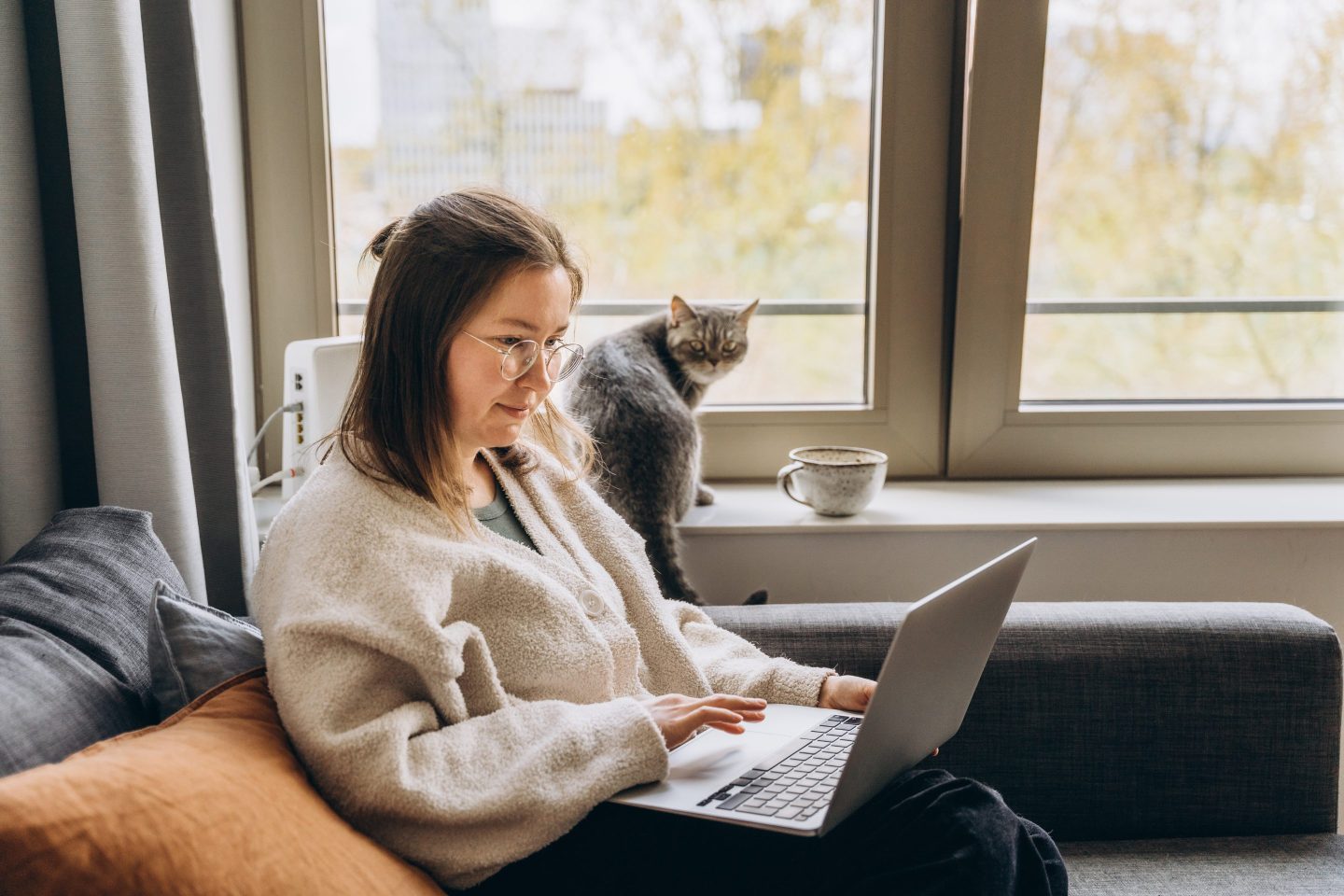 A young woman uses a laptop while sitting on the sofa.