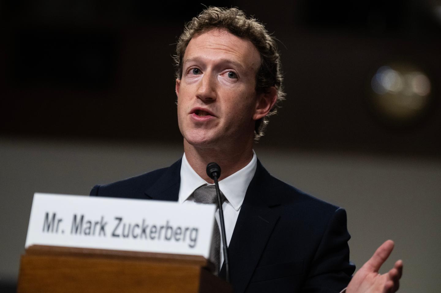 Close up of Mark Zuckerberg speaking with a white name sign in front of him.