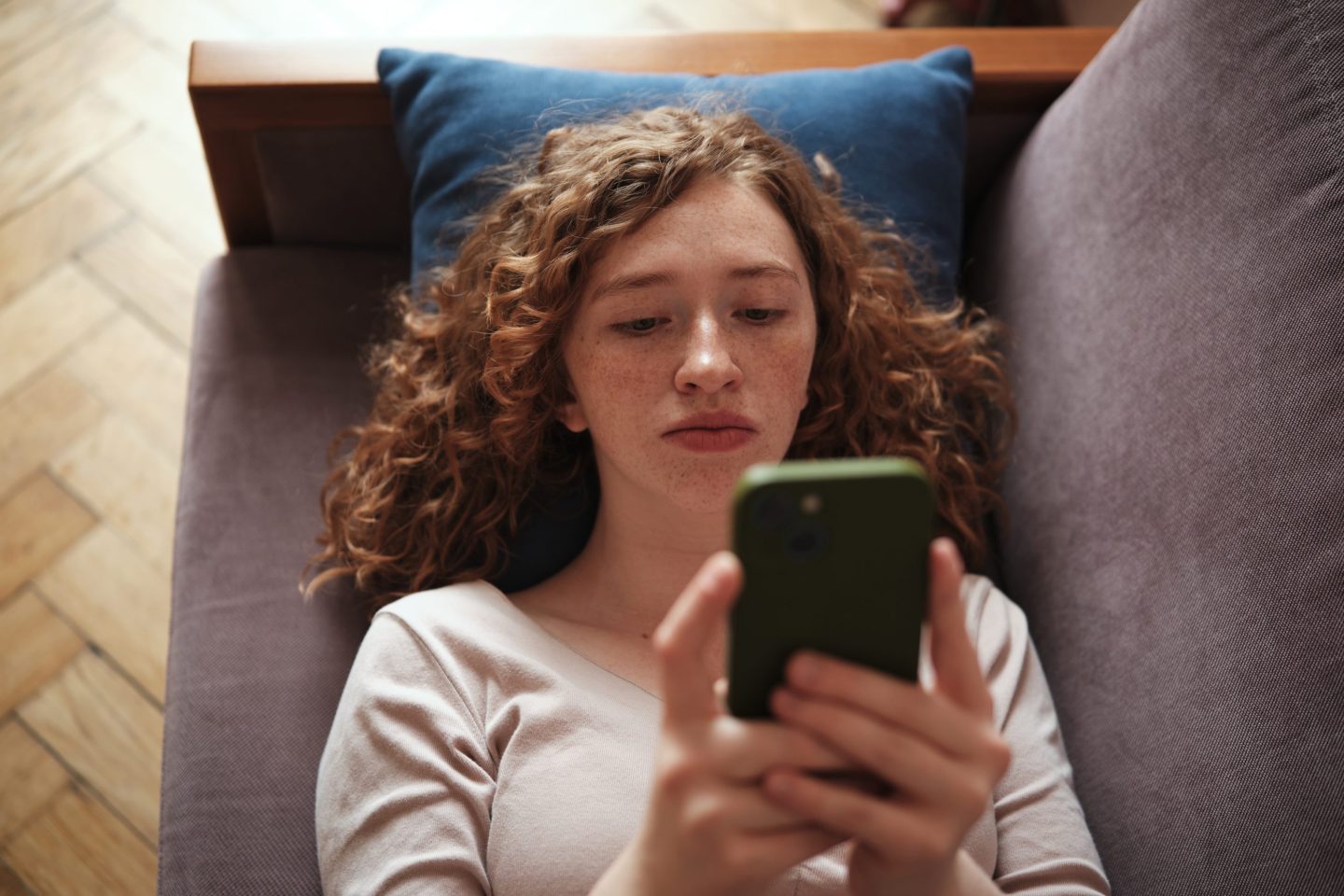 Young adult lays on a couch looking at a cell phone