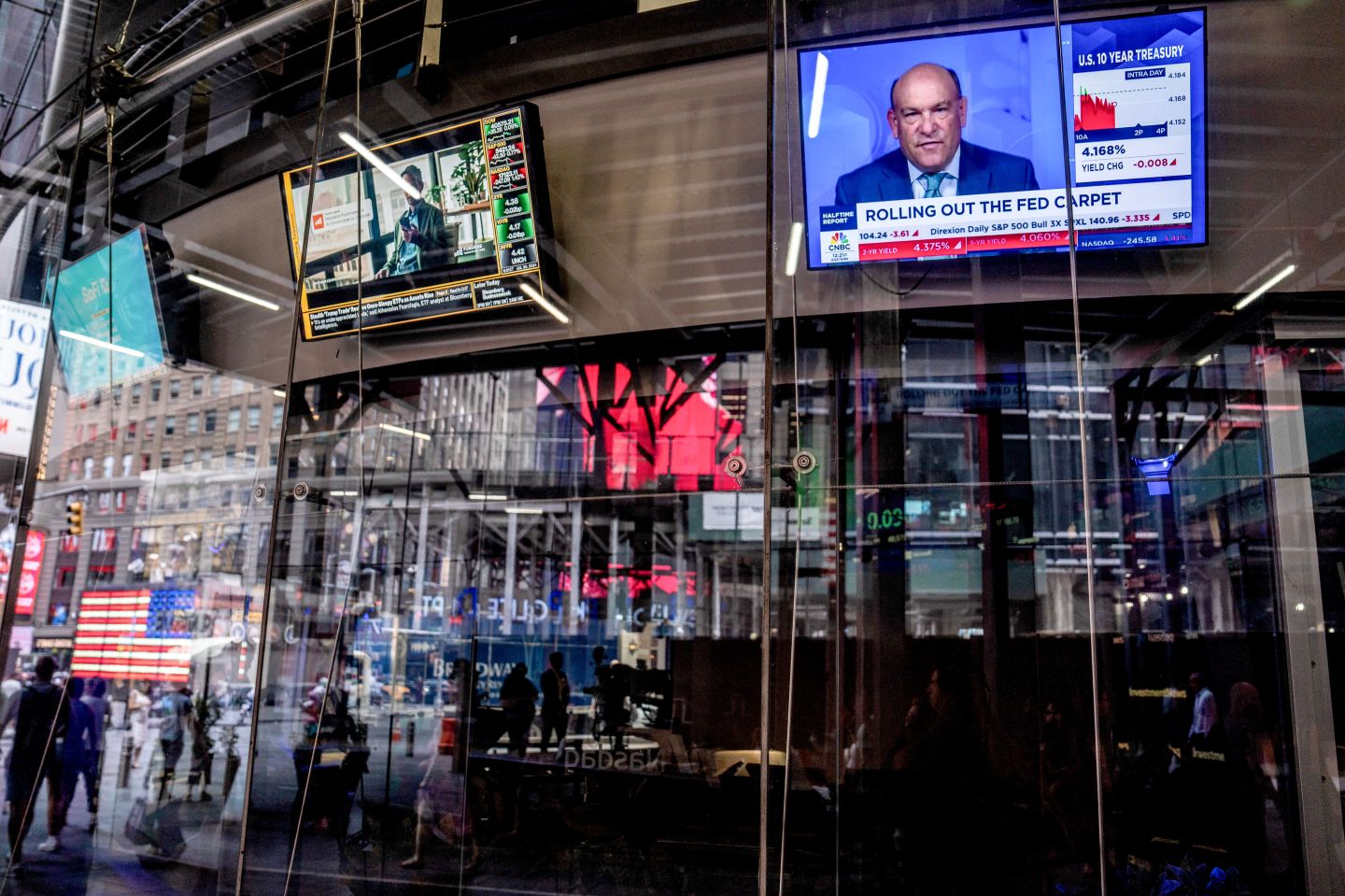 A trader sits inside a glass building with the news playing on screens around them.