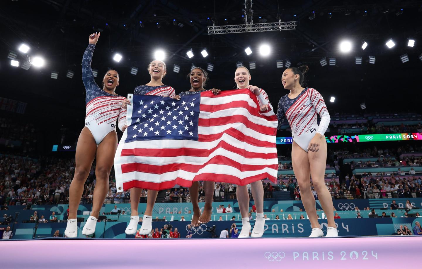 Four gymnasts hold up an American flag