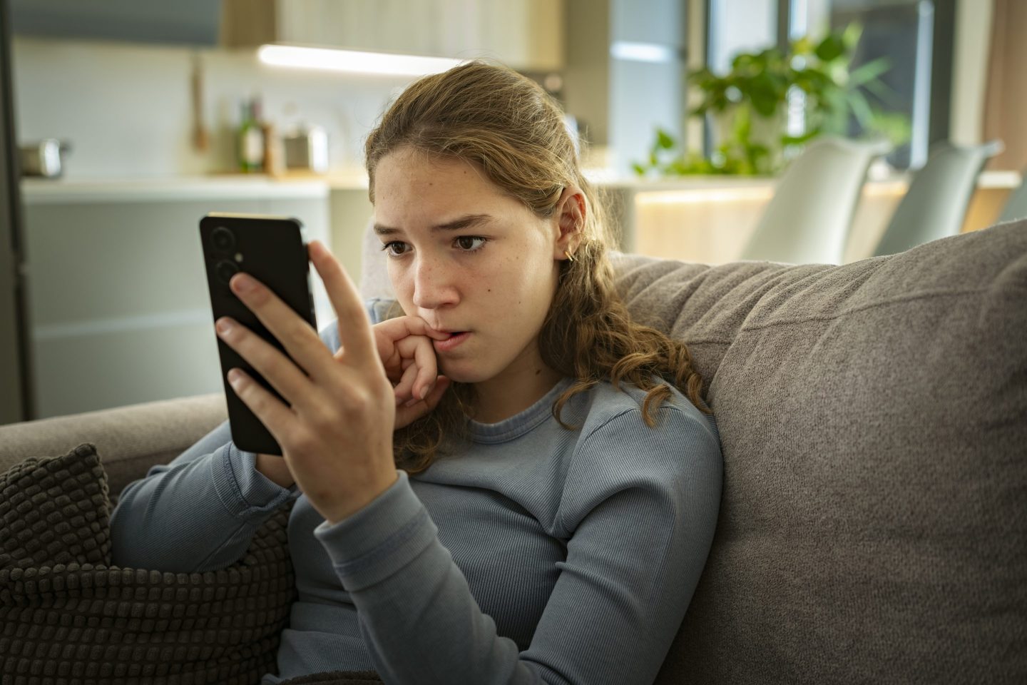 Nervous woman looks at her phone while biting her nail.