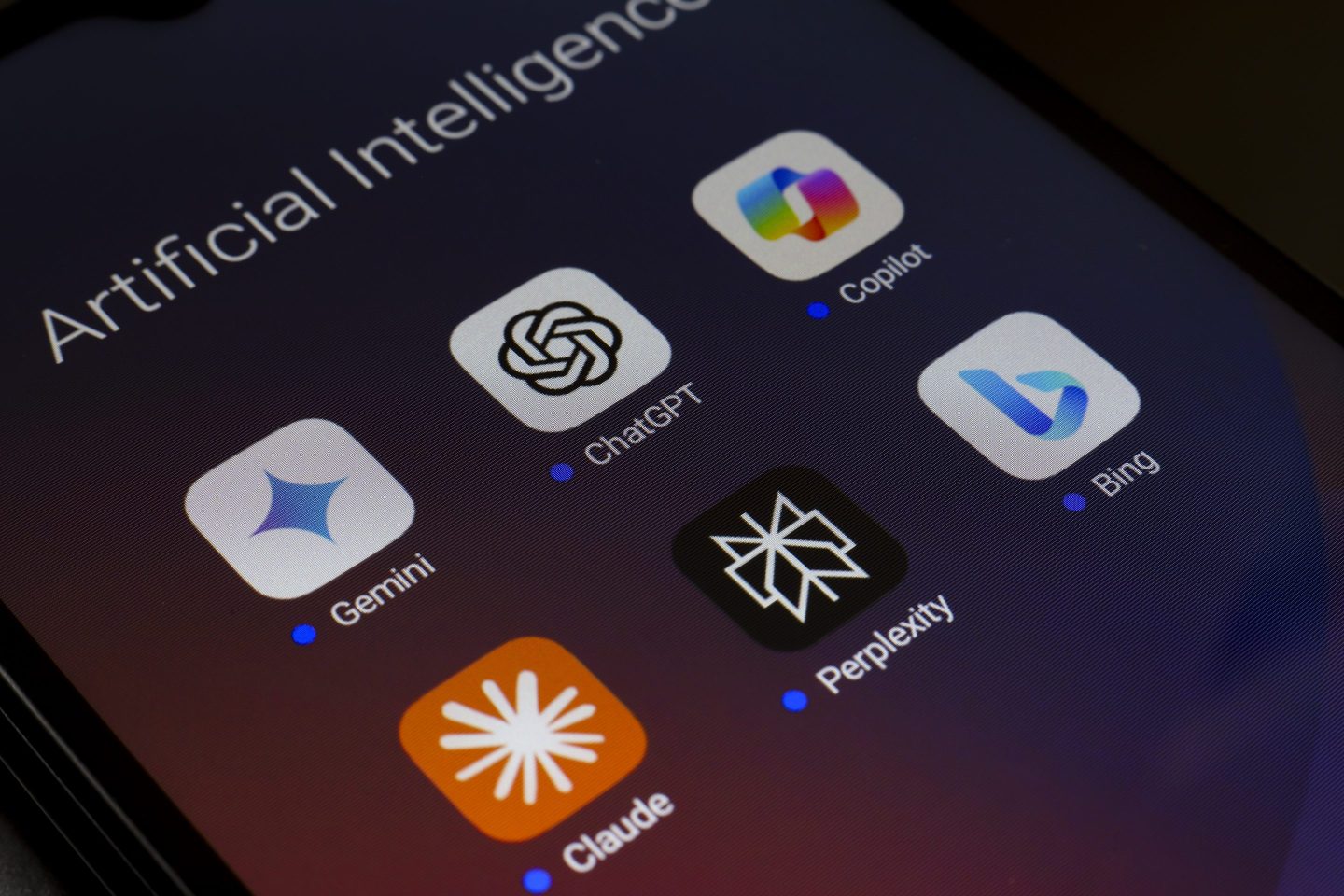 The logos of Google Gemini, ChatGPT, Microsoft Copilot, Claude by Anthropic, Perplexity, and Bing apps are displayed on the screen of a smartphone
