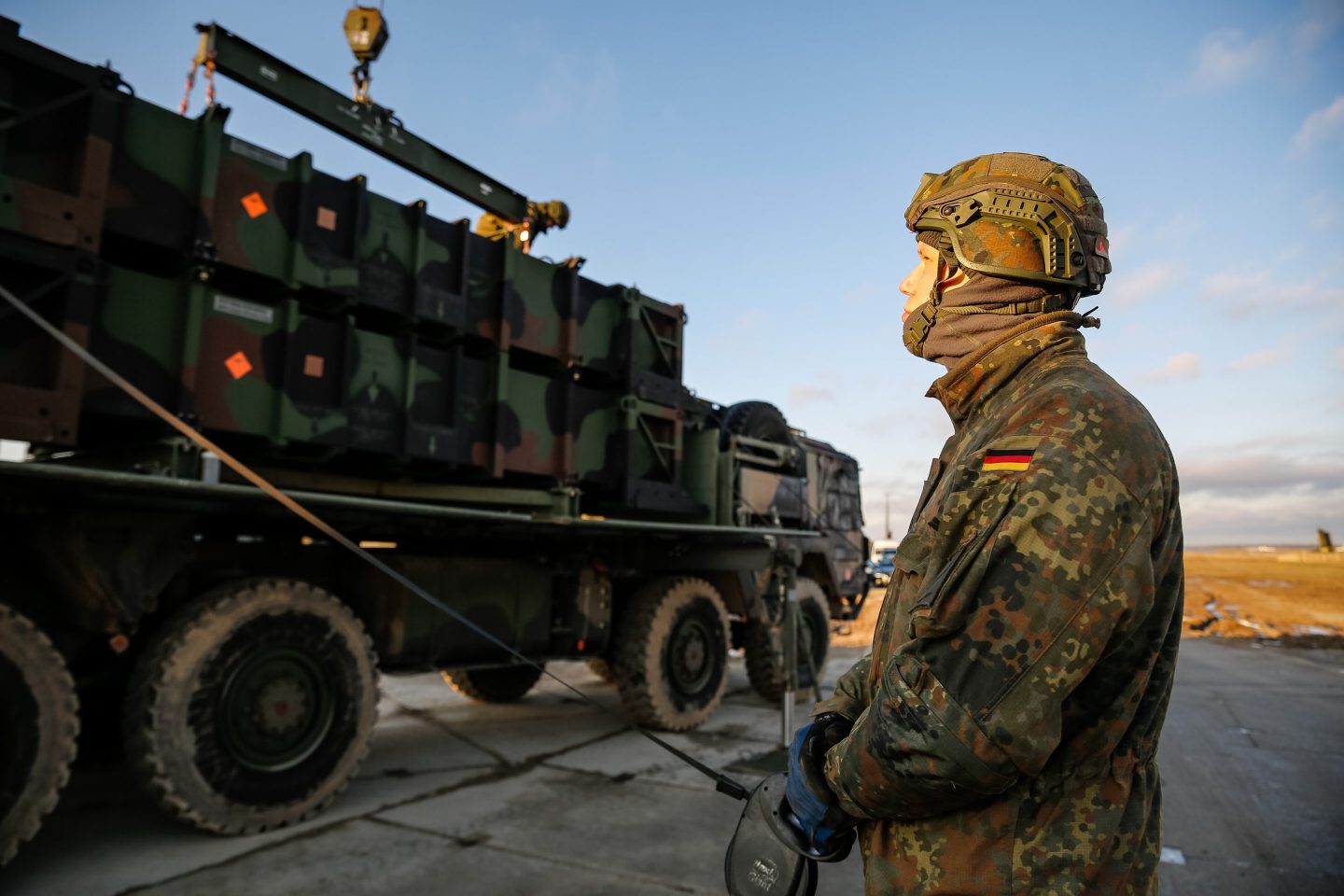 A German soldier looks up as he stands to the side of a large military transport vehicle.