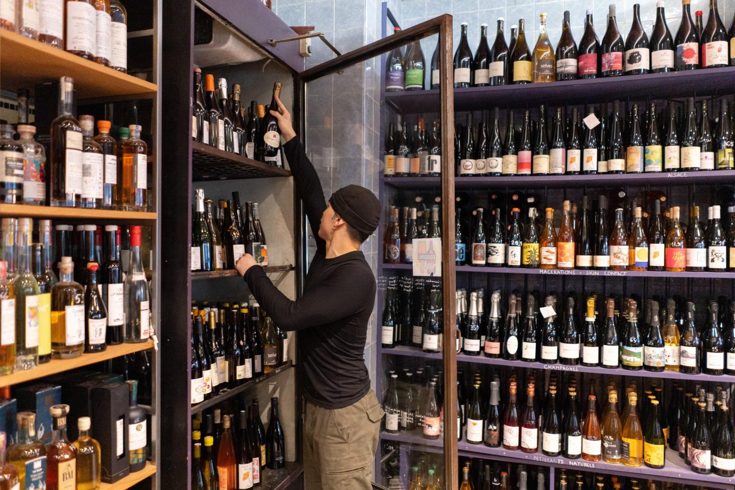 A store attendant takes a bottle of Champagne from a refrigerated display cabinet