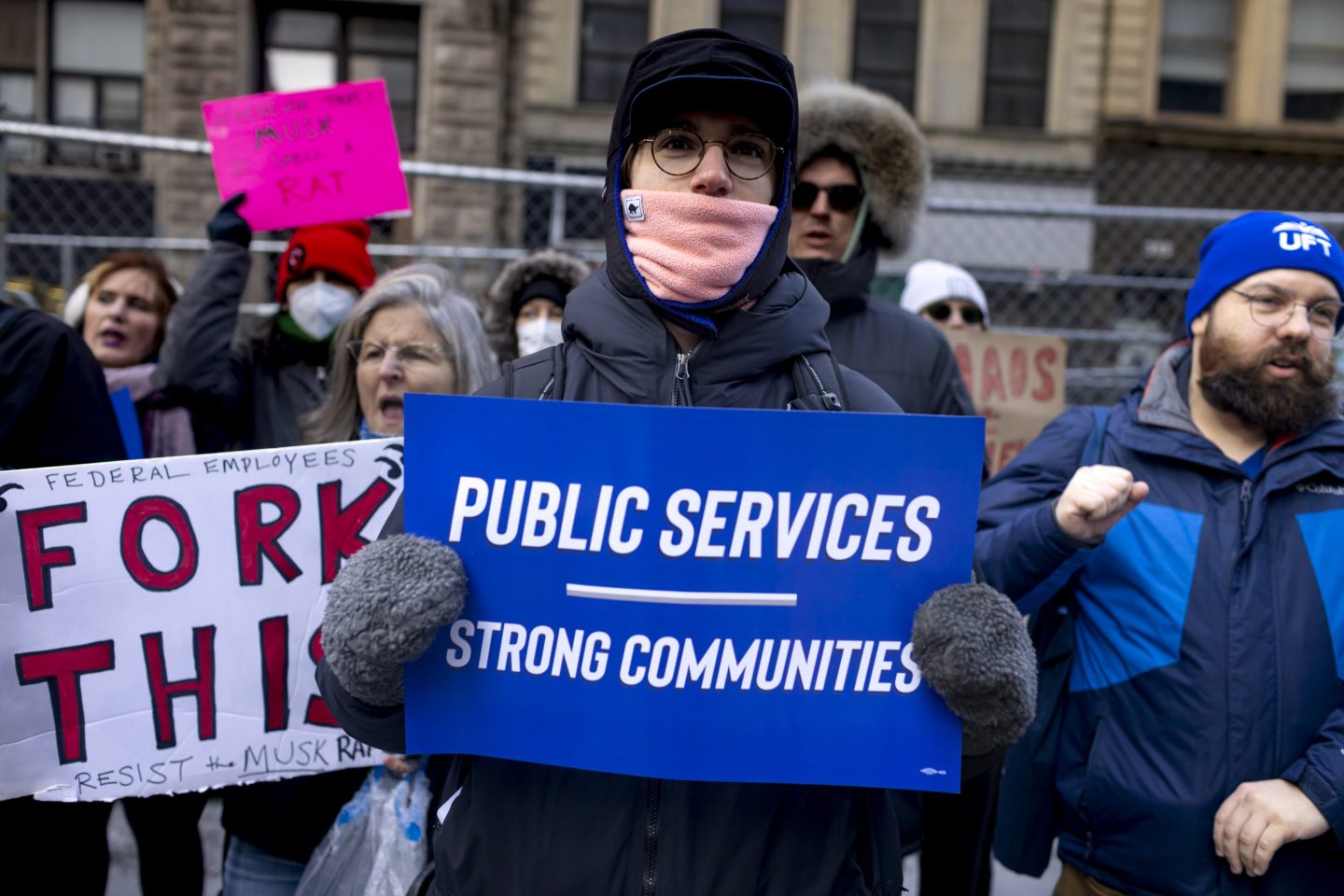 A federal worker protesting the firing of government employees, holding a sign saying "public services, strong communities."