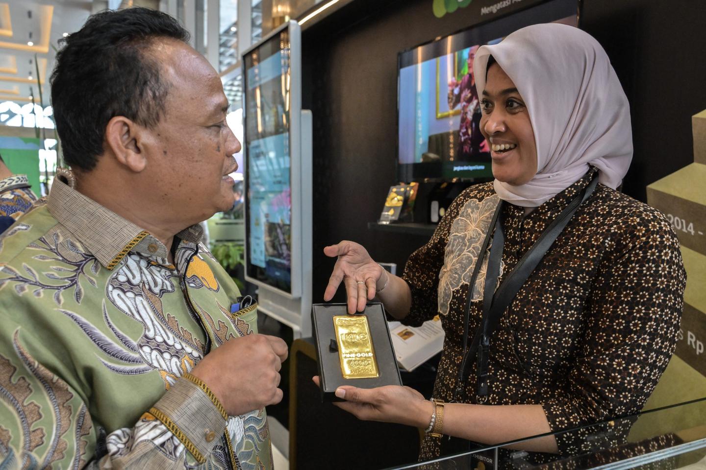 A staff member holds out a bar of gold bullion to a potential buyer.