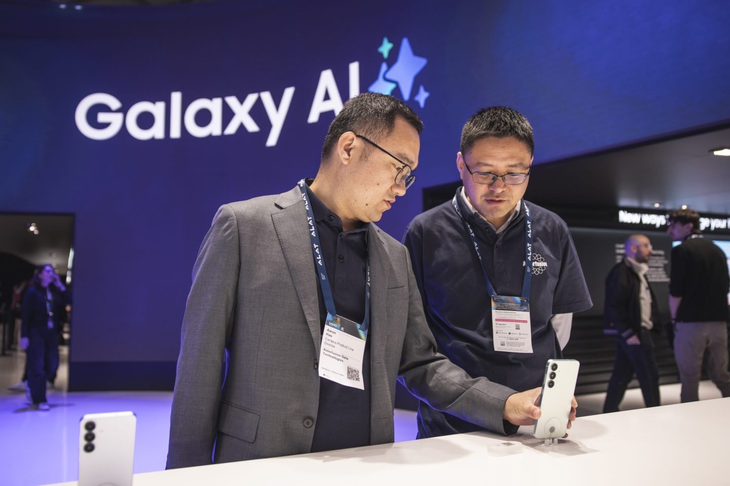 Two mean attending Mobile World Congress 2025 in Barcelona looking at a new Samsung Galaxy phone on display at on a table, while in the background a sign reads "Galaxy AI"
