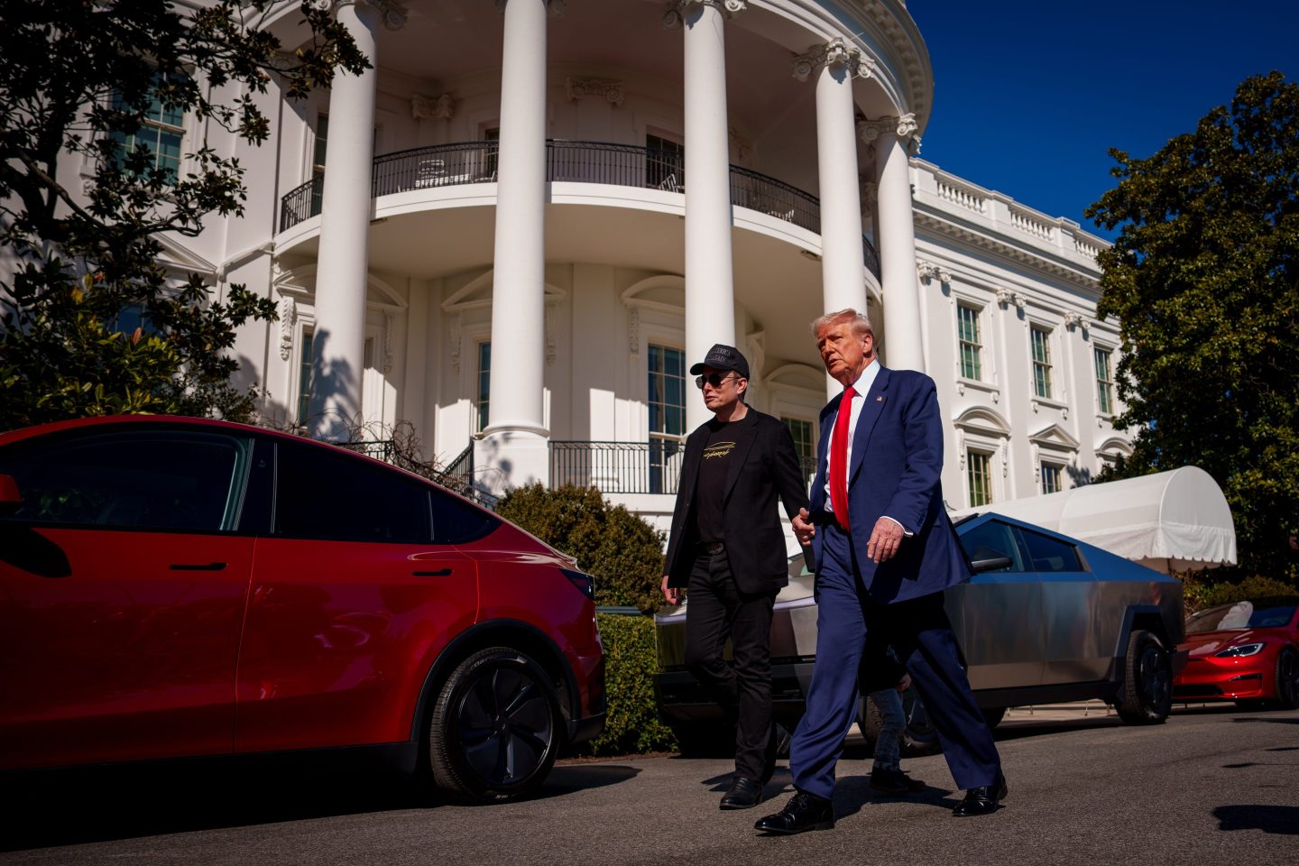Elon Musk and Donald Trump walk past Tesla vehicles parked outside the White House