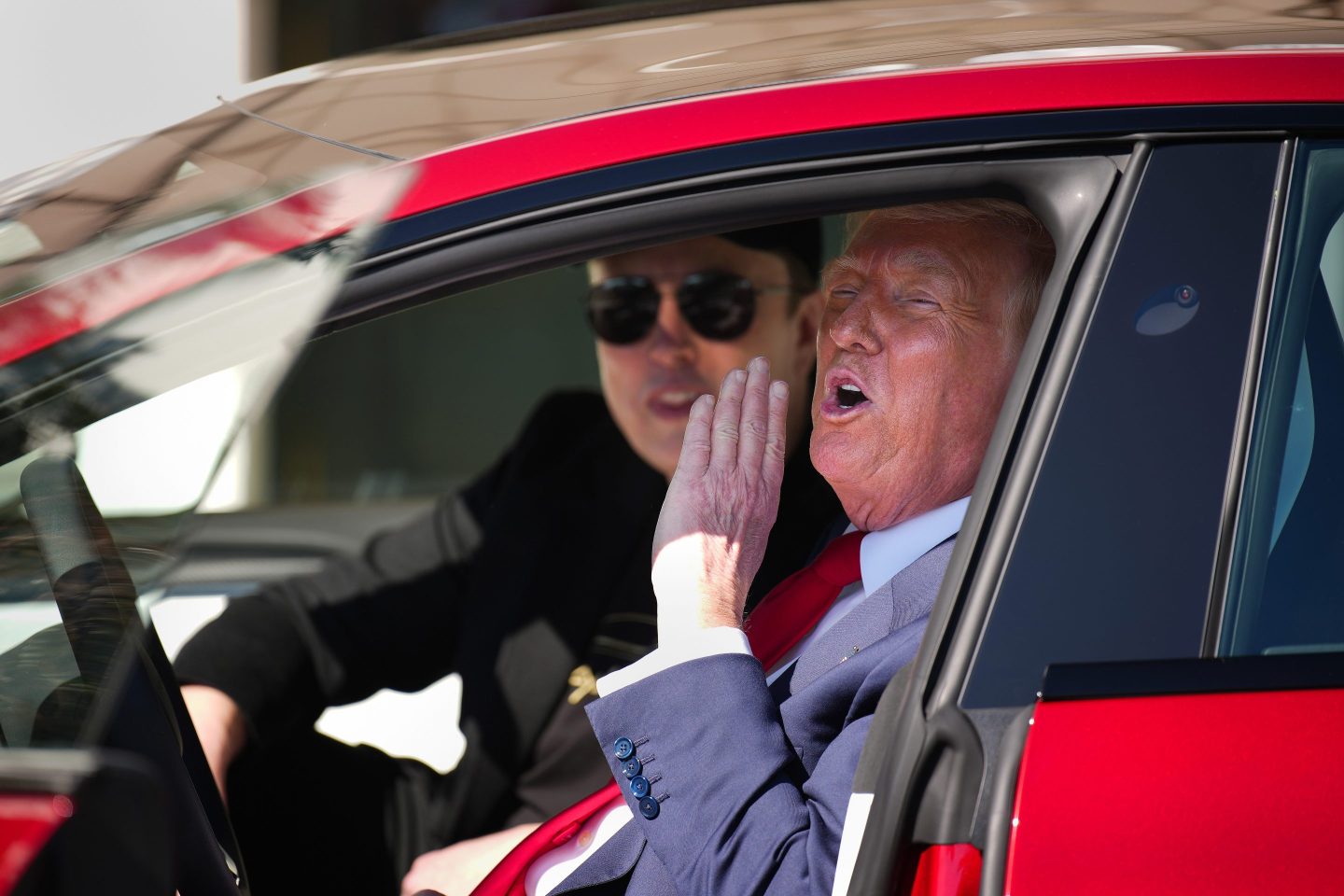Trump hollers out the window of a Tesla with Elon Musk sitting next to him