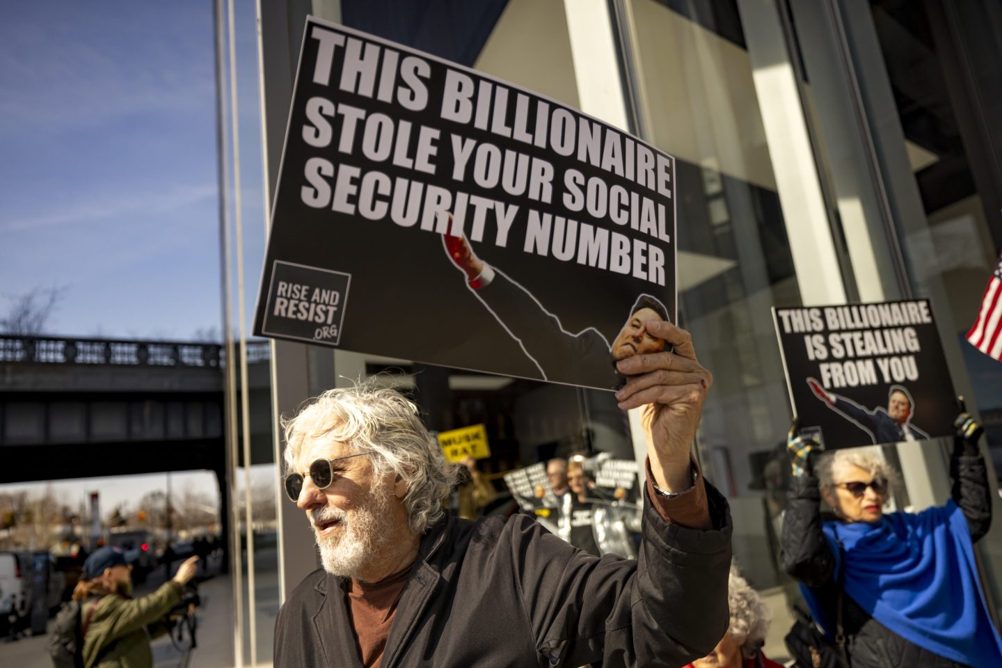 A protester holds signs that read: "This billionaire stole your social security number" during a protest
