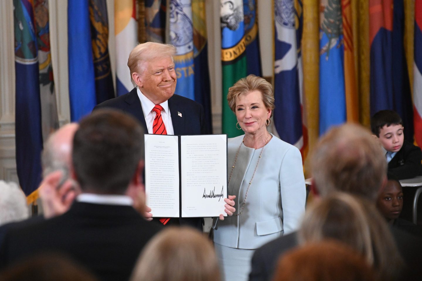 President Donald Trump holding up a signed executive order poses with U.S. Education Secretary Linda McMahon
