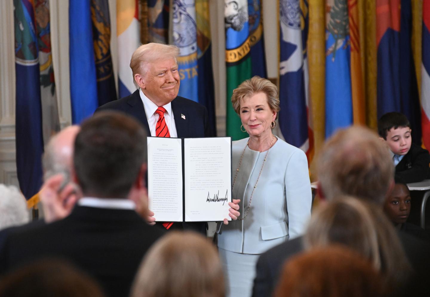 President Donald Trump holding up a signed executive order poses with U.S. Education Secretary Linda McMahon