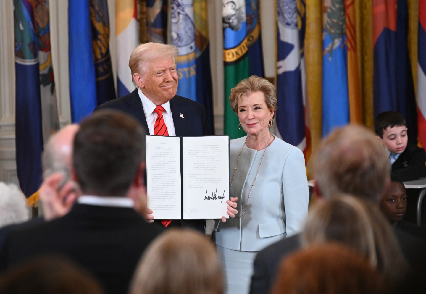 President Donald Trump holding up a signed executive order poses with U.S. Education Secretary Linda McMahon