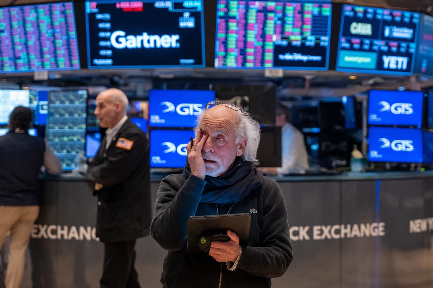 A man covers the right side of his face with his hand in apparent distress on the floor of the New York Stock Exchange.