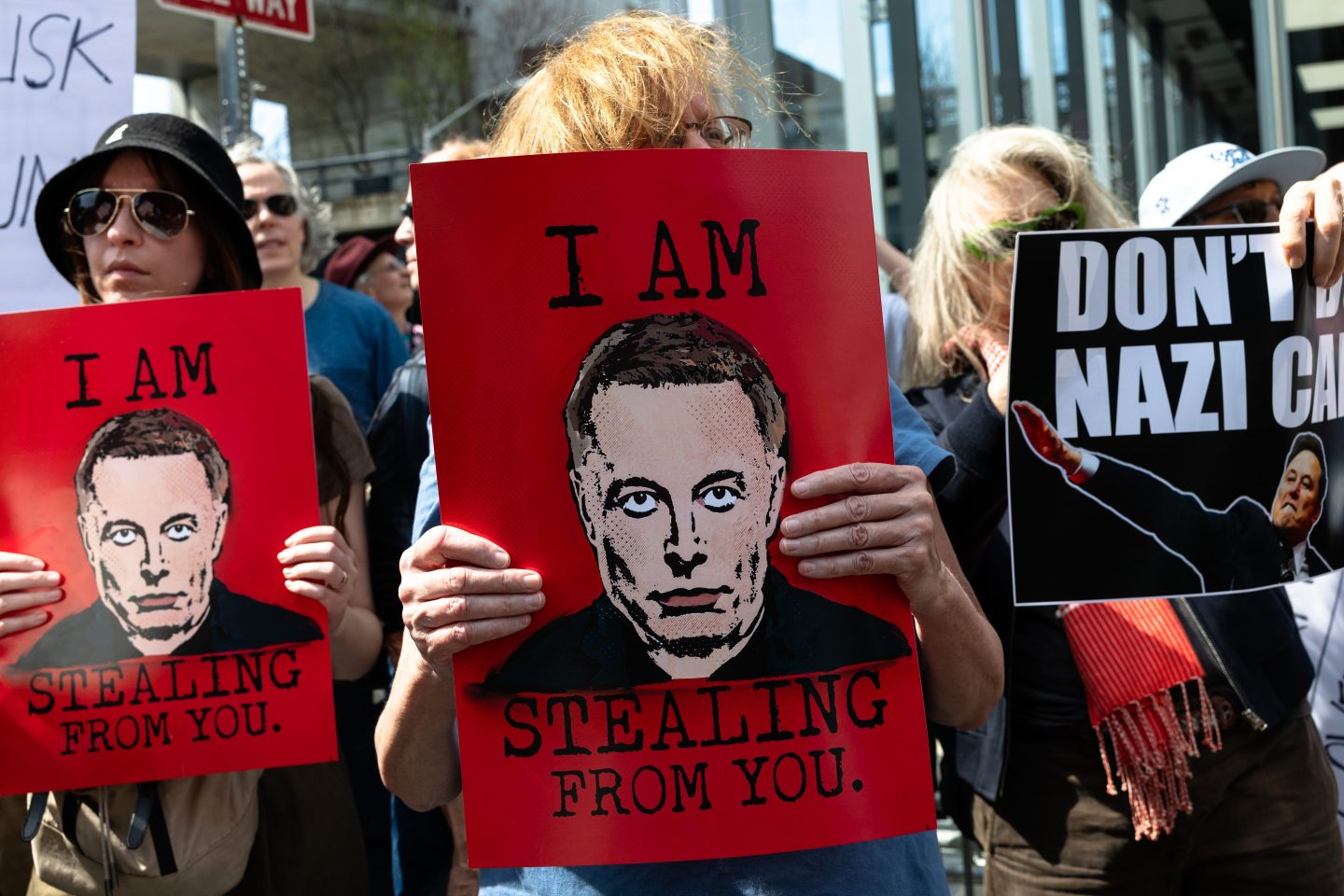 People holding signs and protesting in front of a Tesla dealership