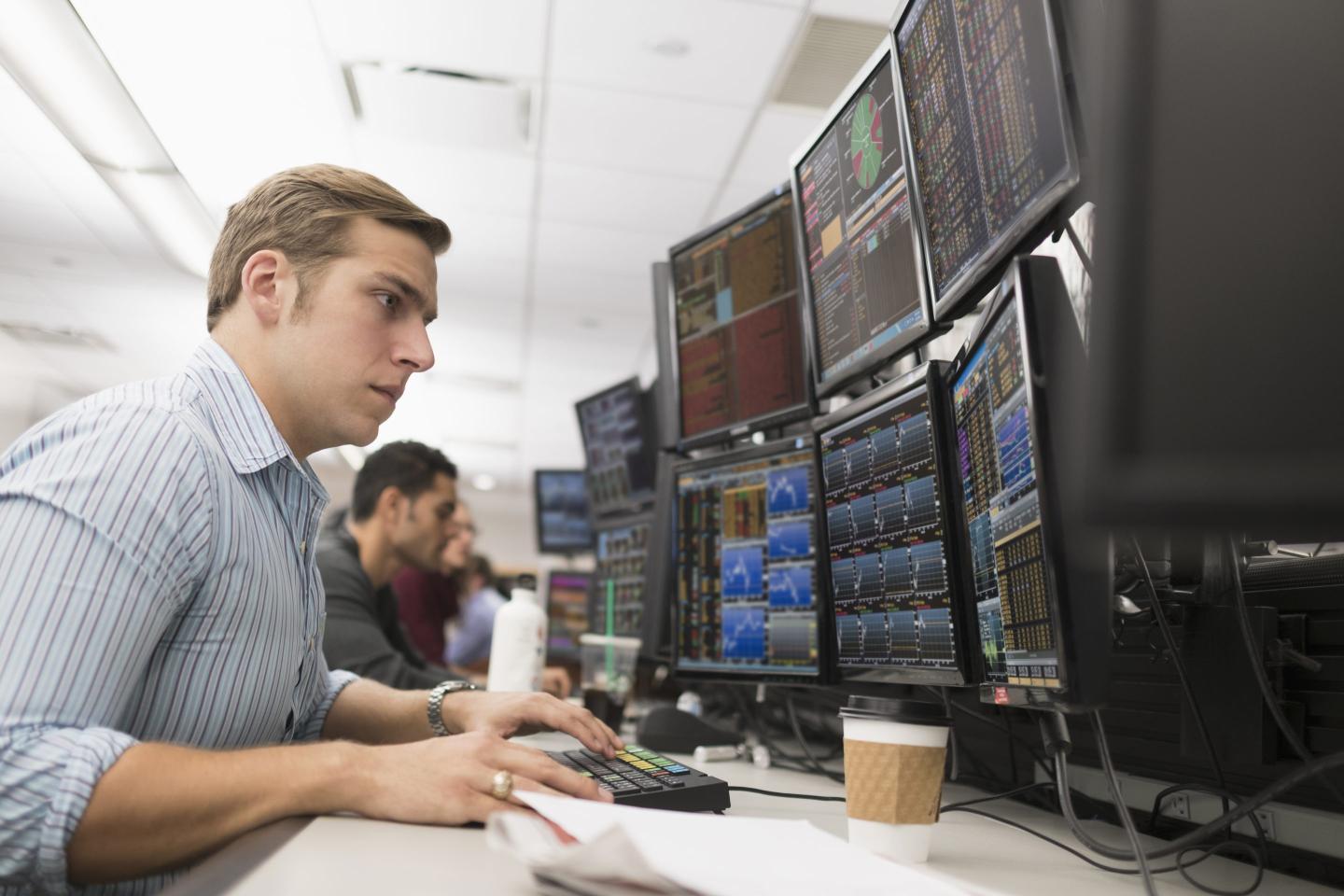 A young trader analyzes data on multiple computer screens