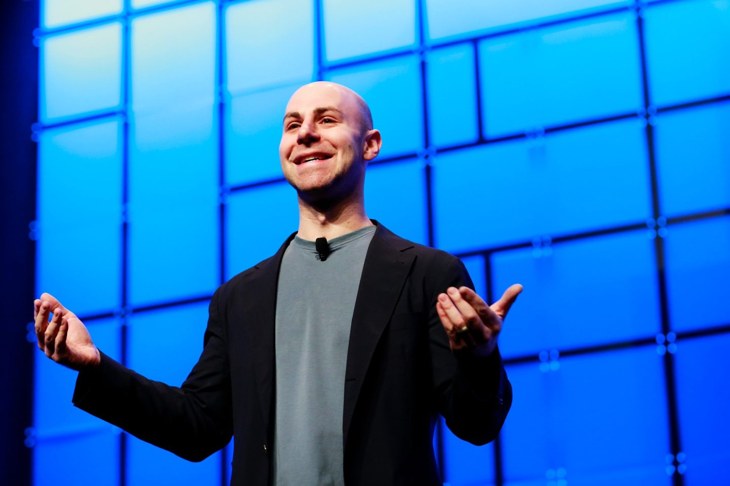 Adam Grant is standing on stage with his arms open during a presentation.