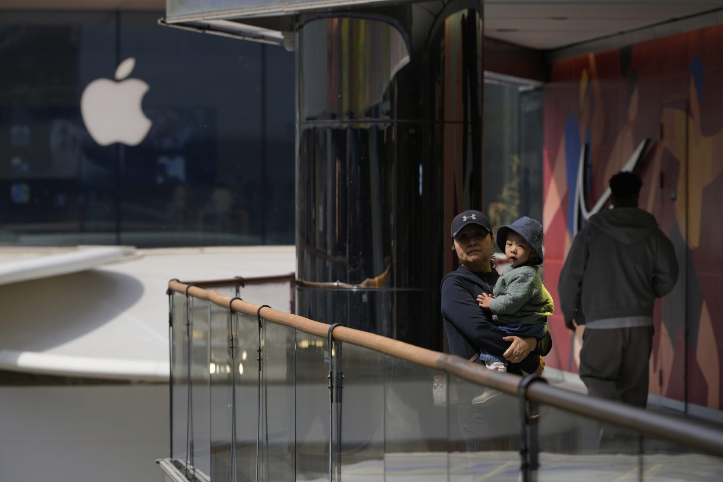 A woman carrying a child stands near Apple and Nike stores in Beijing, China, on April 4, 2025.