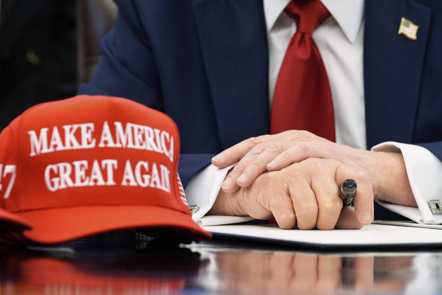 A shot of Trump's hands folded on the Resolute Desk, with a MAGA hat next to them