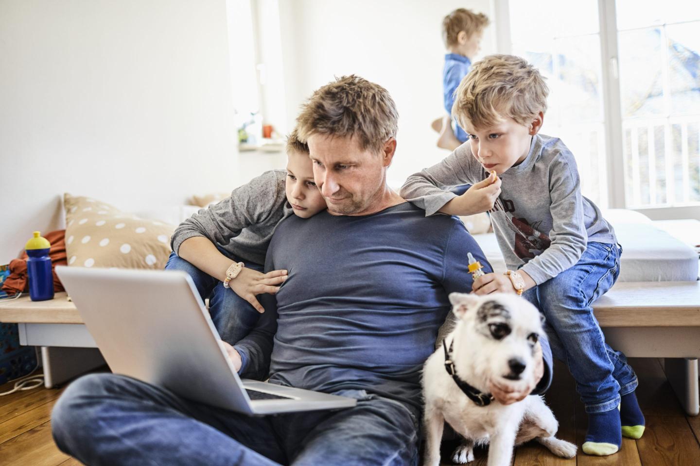 Father using laptop at home with children watching - stock photo