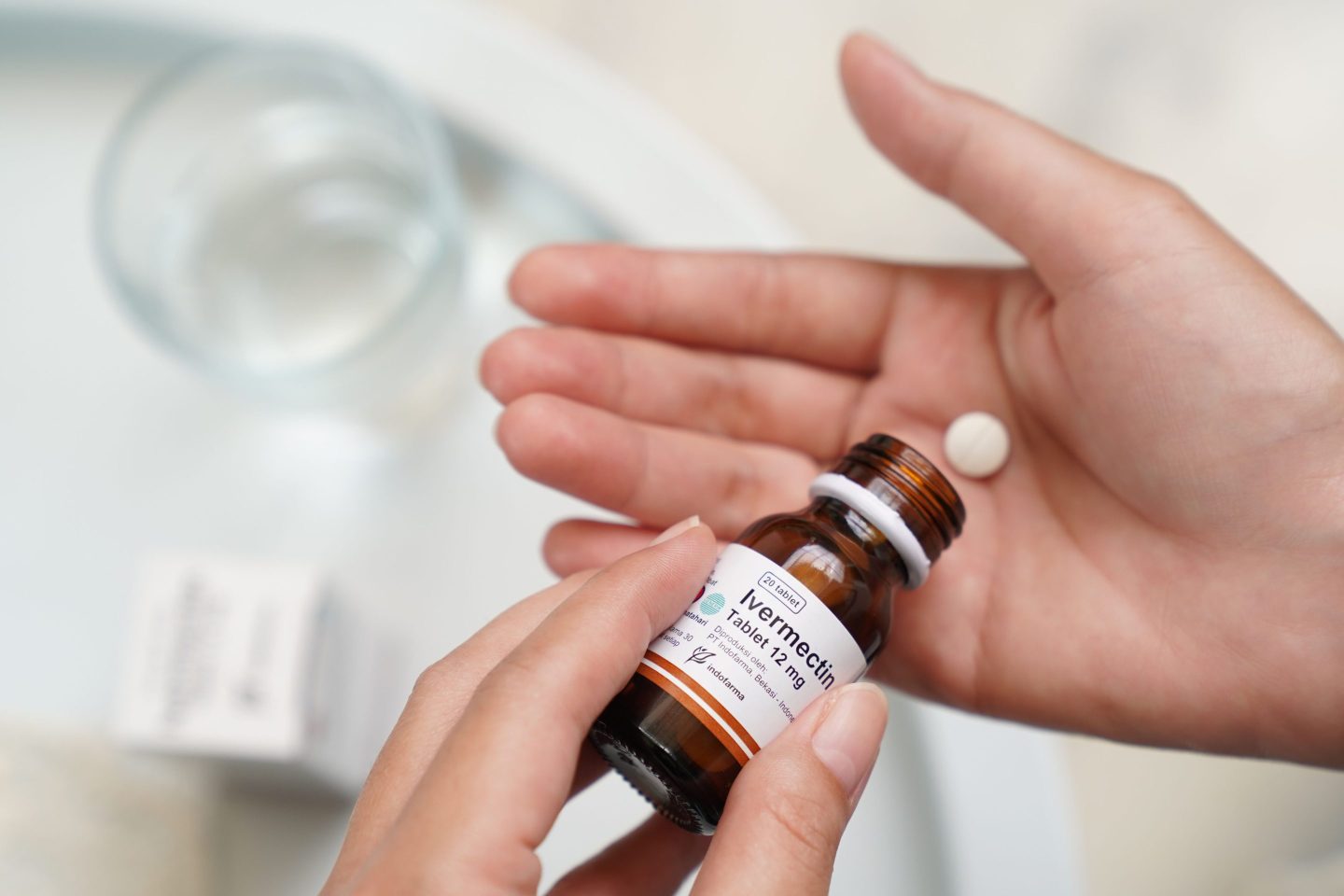 A hand holding an Ivermectin tablet, with the bottle in the other hand