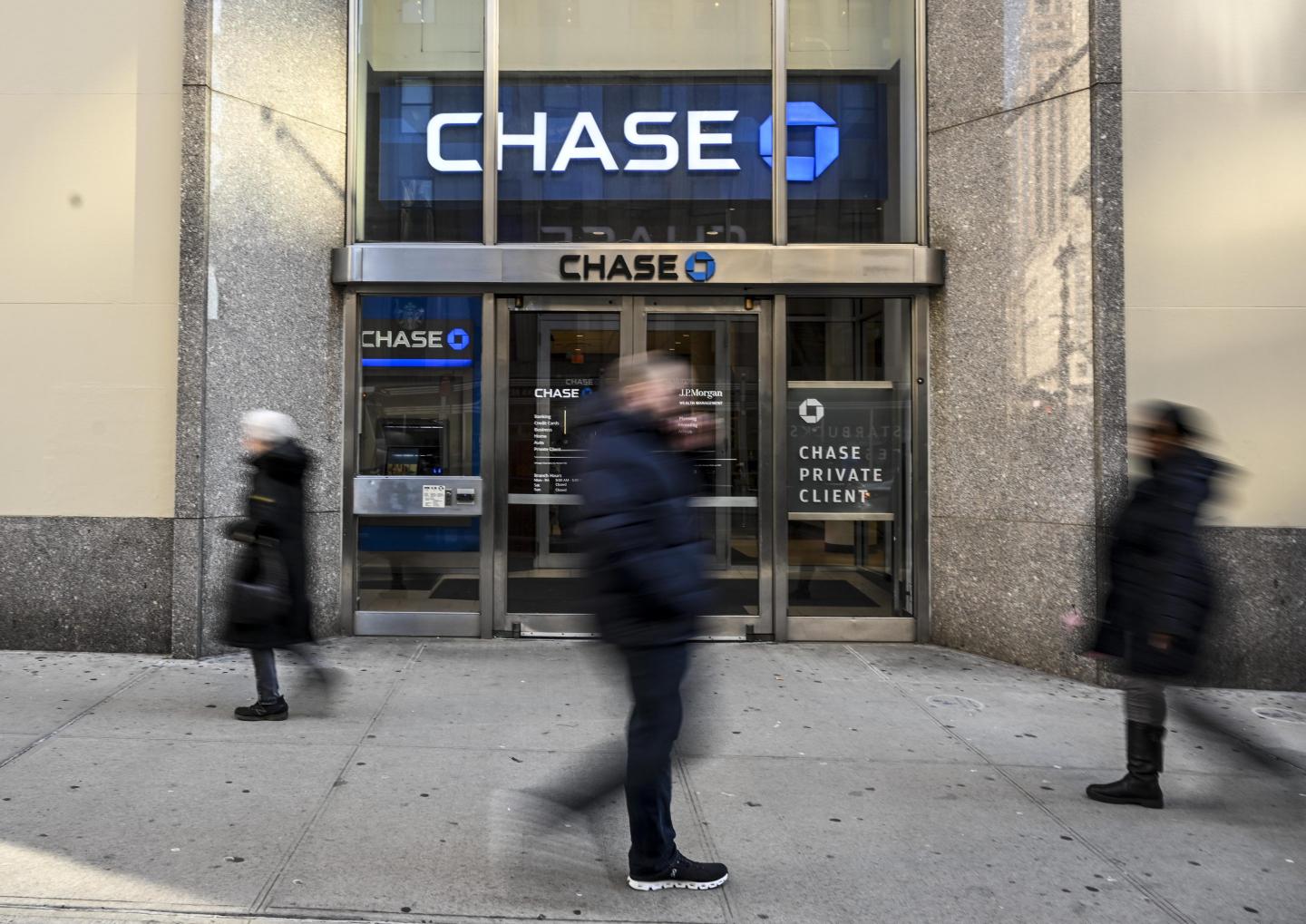 People on the sidewalk walk past a Chase bank.