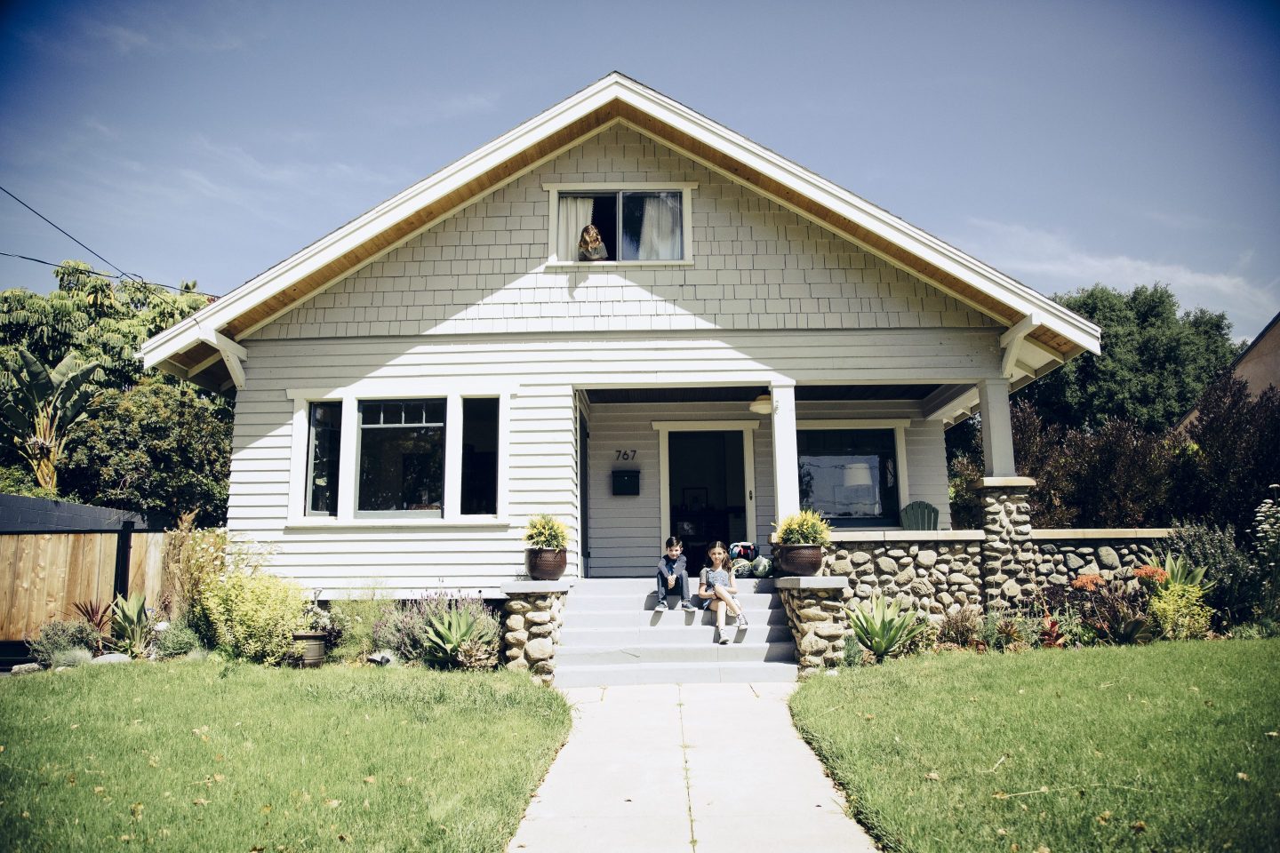 Brother and sister sitting on front step at home on sunny day