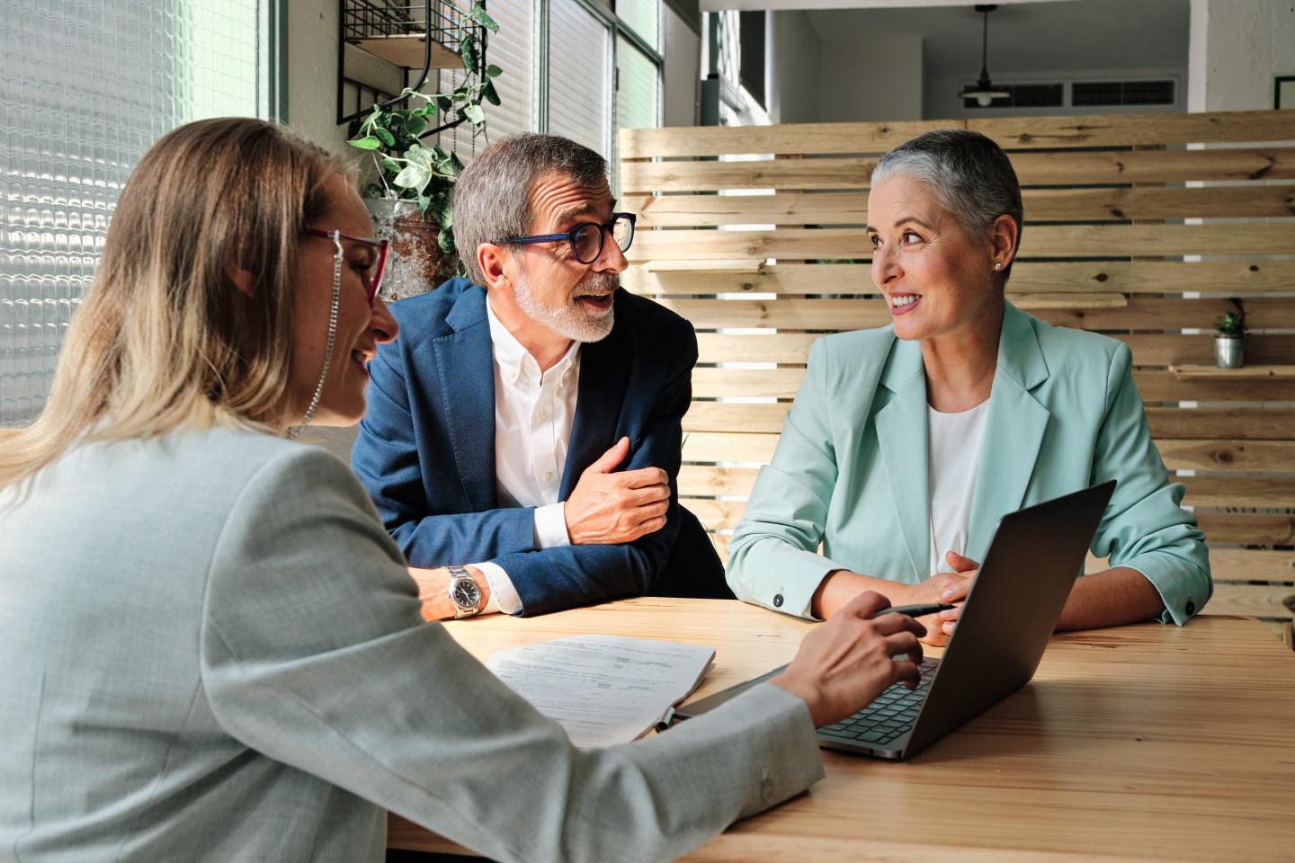 A financial advisor points at a computer as a man and woman on the other side of the table smile and look at each other.