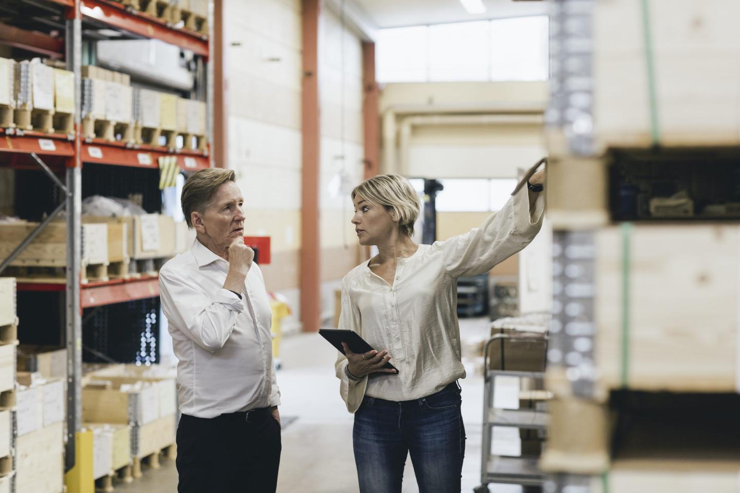 Female manger explaining senior businessman in factory warehouse.